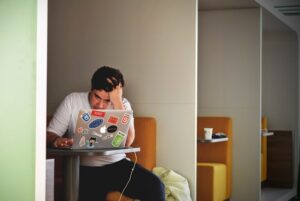 Homem em co-working, ohando para a tela do laptop com expressão de preocupado.