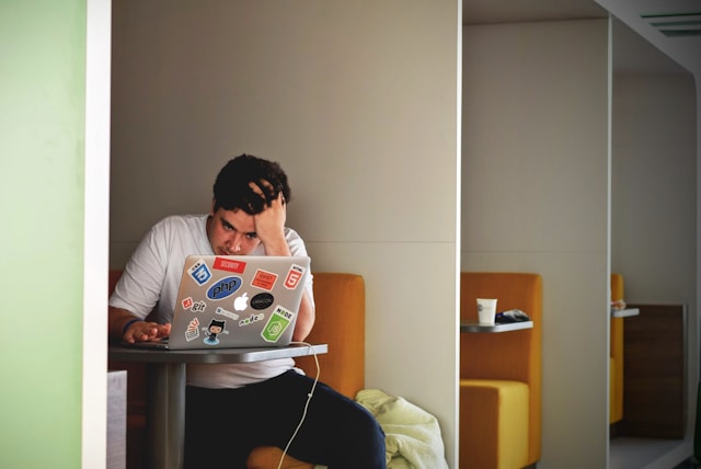 Homem em co-working, ohando para a tela do laptop com expressão de preocupado.